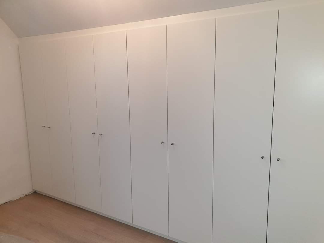 Wand met witte inbouwkasten over de volledige breedte van de kamer
